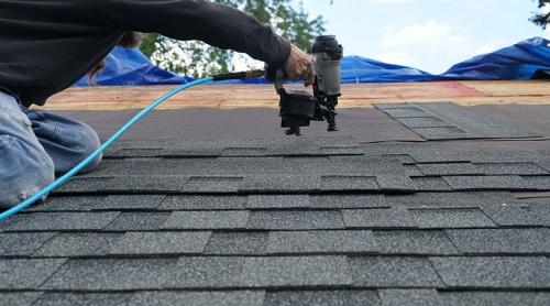 handyman using nail gun to install shingle to repair roof